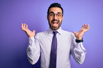 Handsome businessman with beard wearing casual tie and glasses over purple background celebrating crazy and amazed for success with arms raised and open eyes screaming excited. Winner concept