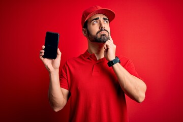 Young handsome delivery man with beard holding smartphone showing deliver food app serious face thinking about question, very confused idea