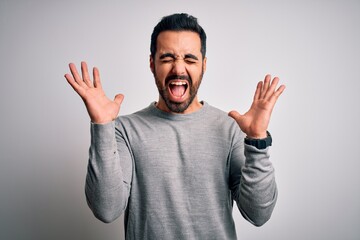 Fototapeta premium Young handsome man with beard wearing casual sweater standing over white background celebrating mad and crazy for success with arms raised and closed eyes screaming excited. Winner concept