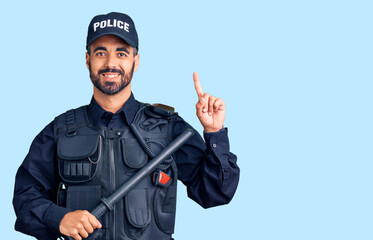 Young hispanic man wearing police uniform holding baton surprised with an idea or question pointing...