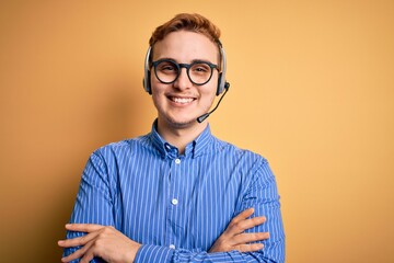 Young handsome redhead call center agent man wearing glasses working using headset happy face smiling with crossed arms looking at the camera. Positive person.