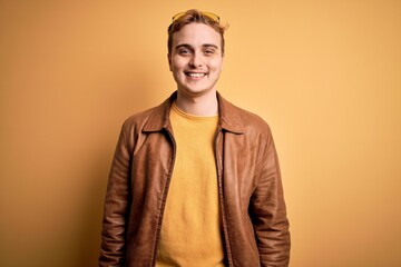 Young handsome redhead man wearing casual leather jacket over isolated yellow background with a happy and cool smile on face. Lucky person.