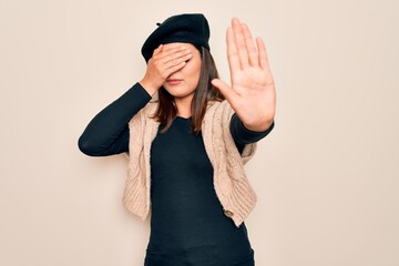 Young beautiful brunette woman wearing casual french beret over white background covering eyes with hands and doing stop gesture with sad and fear expression. Embarrassed and negative concept. © Krakenimages.com