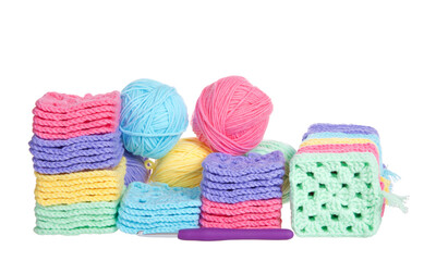 Piles of colorful hand crochet granny squares with balls of yarn piled behind, crochet hook laying in front. Isolated on white background.