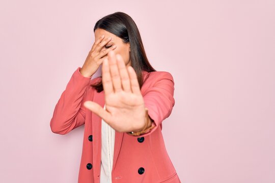 Young beautiful brunette businesswoman wearing elegant jacket over isolated pink background covering eyes with hands and doing stop gesture with sad and fear expression. Embarrassed and negative.
