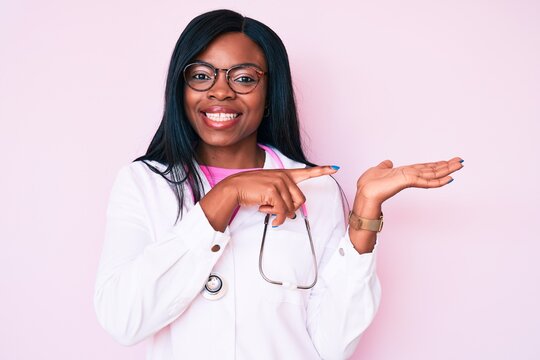 Young african american woman wearing doctor stethoscope amazed and smiling to the camera while presenting with hand and pointing with finger.