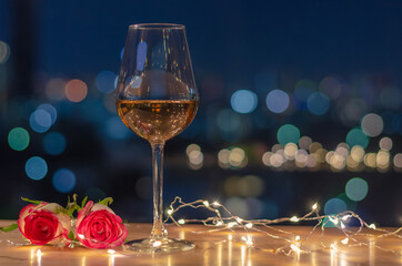 A glass of Rose wine with rose flowers on table and colorful city bokeh light background.