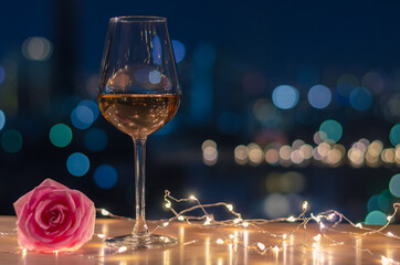 A glass of Rose wine with rose flower on table and colorful city bokeh light background.