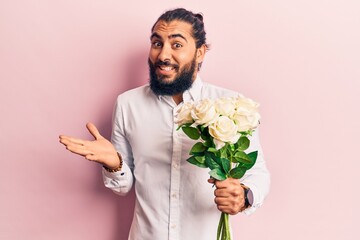 Young arab man holding flowers celebrating achievement with happy smile and winner expression with raised hand