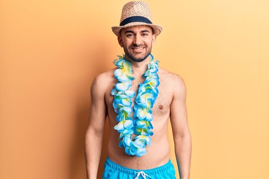 Young handsome bald man shirtless wearing swimwear and hawaiian lei with a happy and cool smile on face. lucky person.
