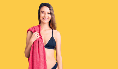 Young beautiful girl wearing bikini and beach towel looking positive and happy standing and smiling with a confident smile showing teeth