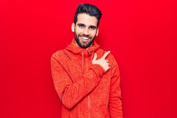 Young handsome man with beard wearing casual sweatshirt smiling cheerful pointing with hand and finger up to the side