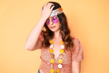 Young beautiful brunette woman wearing bohemian and hippie style surprised with hand on head for...