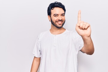 Naklejka premium Young hispanic man wearing casual clothes showing and pointing up with finger number one while smiling confident and happy.