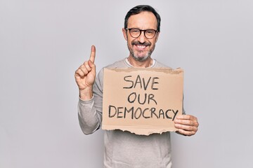 Middle age man holding banner with saver our democracy message over white background smiling with an idea or question pointing finger with happy face, number one