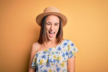 Young beautiful woman wearing casual t-shirt and summer hat over isolated yellow background winking looking at the camera with sexy expression, cheerful and happy face.