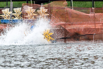 Mechanical water aerator installed in a fishing pond. The technology improves the metabolism of fish and increases the level of oxygen in the reservoir. Yellow water wheel and flying spray.