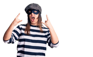 Young beautiful brunette woman wearing burglar mask shouting with crazy expression doing rock symbol with hands up. music star. heavy concept.