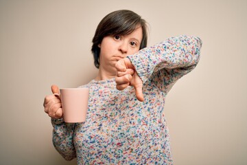 Young down syndrome woman drinking a cup of hot coffee over isolated background with angry face,...