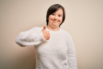 Young down syndrome woman standing over isolated background doing happy thumbs up gesture with hand. Approving expression looking at the camera showing success.