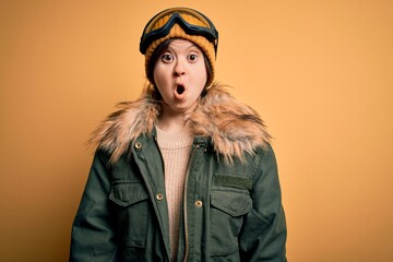 Young down syndrome woman wearing ski coat and glasses for winter weather afraid and shocked with surprise expression, fear and excited face.