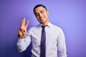 Young brazilian businessman wearing elegant tie standing over isolated purple background showing and pointing up with fingers number three while smiling confident and happy.