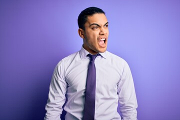 Young brazilian businessman wearing elegant tie standing over isolated purple background angry and mad screaming frustrated and furious, shouting with anger. Rage and aggressive concept.