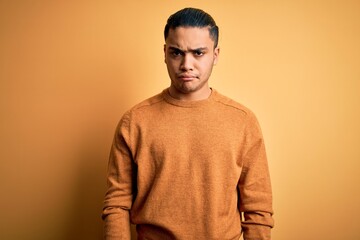 Young brazilian man wearing casual sweater standing over isolated yellow background skeptic and nervous, frowning upset because of problem. Negative person.