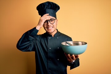 Young brazilian chef man wearing cooker uniform and hat using bowl and whisk stressed with hand on...