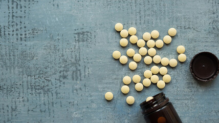 yellow round tablets or pills vitamins on blue stone concrete table with black plastic bottle, side...