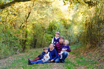 Fototapeta na wymiar Portrait of young parents with three children. Mother, father, two kids brothers boys and little cute toddler sister girl having fun together in autumn forest. Happy family of five