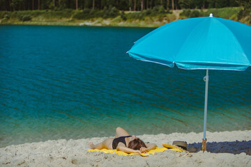 Fototapeta na wymiar woman laying on yellow blanket at sand beach with blue sun umbrella