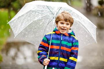 Beautiful little kid boy on way to school walking during sleet, rain and snow with an umbrella on...