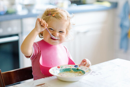 Adorable baby girl eating from spoon vegetable noodle soup. food, child, feeding and development concept. Cute toddler child, daughter with spoon sitting in highchair and learning to eat by itself