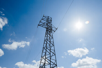 Metal high-voltage tower on a background of blue sky with white clouds. Power supply