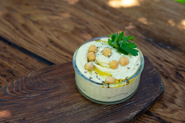 Classic hummus appetizer of chickpeas, tahini, olive oil, and oriental spices in a bowl on a wooden table. Traditional Mediterranean vegetarian snack.