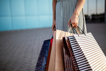 Closeup of young attractive woman holding a few shopping bags with newly purchased goods and clothes. Girl holds colourful packs full of bought things in her hands. Shopping and spendings concept.