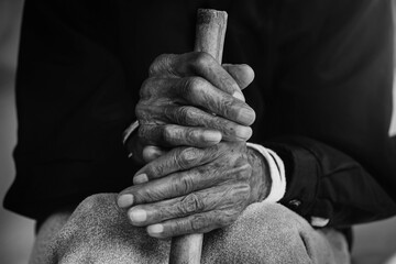 Asian old man sitting with his hands on a walking stick.