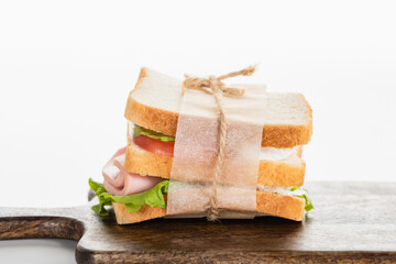 fresh delicious sandwich with sliced sausage and lettuce on wooden cutting board on white surface