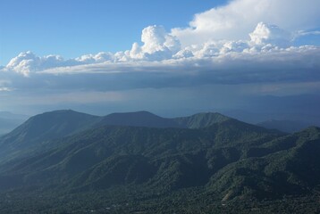 view of an non active volcano, full of vegetation and a blue sky with many clouds