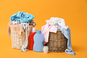 Baskets with dirty clothes and detergents on color background