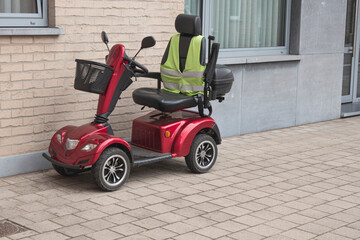 A red four wheel scooter with a yellow fluor vest parked against the facade of a house