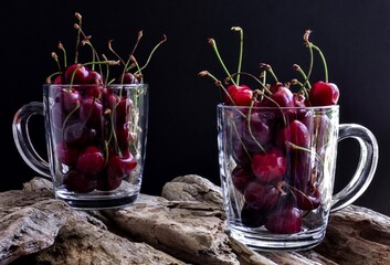 Ripe, red cherries in cups of tea on a wooden background. Dark background.