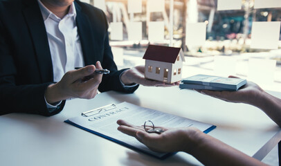 Real estate agent congratulations to new buyer by giving house model to client in the agency office.