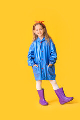 Cute little girl in raincoat on color background