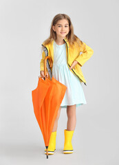 Cute little girl in raincoat and with umbrella  on grey background