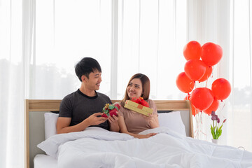 A young couple lovers exchange a gift box with each other on bed in their bedroom.