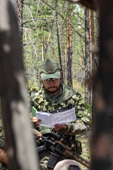 Fully armed american soldier is reviewing a document on military range, active military game...