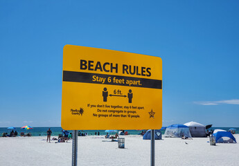A prominent yellow sign illustrating the Beach Rules of social distancing to stay six feet apart. Clearwater Beach, FLorida, USA.