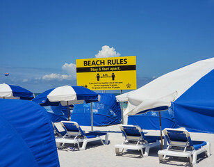 A prominent yellow sign illustrating the Beach Rules of social distancing to stay six feet apart. Clearwater Beach, FLorida, USA.
